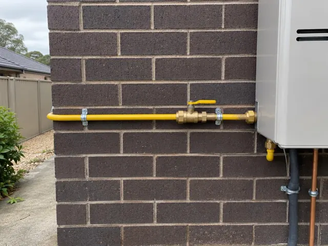 Yellow gas pipe and valve on a brick exterior wall beside a wall-mounted appliance in Kellyville