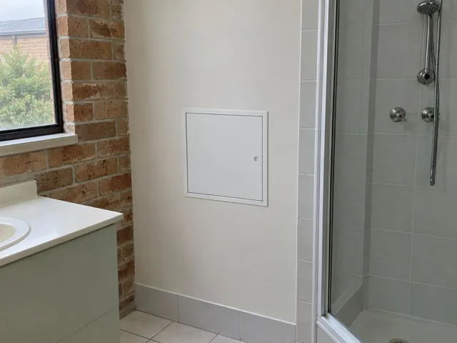 Bathroom wall with small access panel beside a shower and vanity in Beaumont Hills